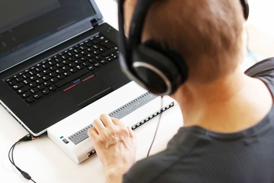 Blind person working on computer with braille display and screen reader